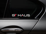 GTHAUS decal displayed on a car window, featuring bold lettering in red and silver on a transparent background.