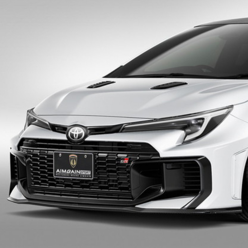White GR Corolla car with a black grille and front bumper Aimgain carbon fiberbody kit on a gray background pmddriven pmd vip website