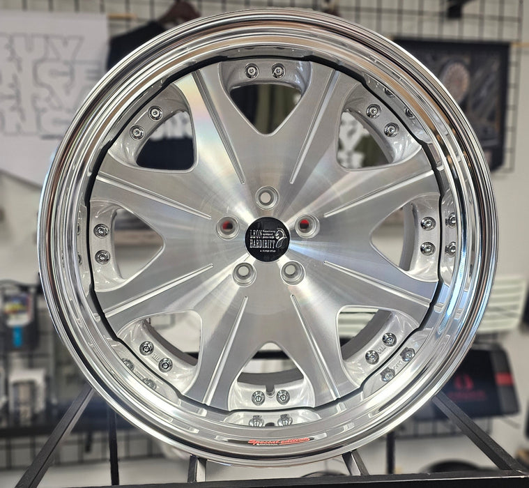 Close-up of a silver alloy wheel on a tiled floor with other wheels in the background.