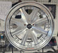 Close-up of a silver alloy wheel on a tiled floor with other wheels in the background.