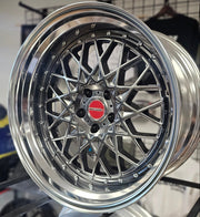 Close-up of a shiny silver car wheel rim with a red logo on a blurred background.