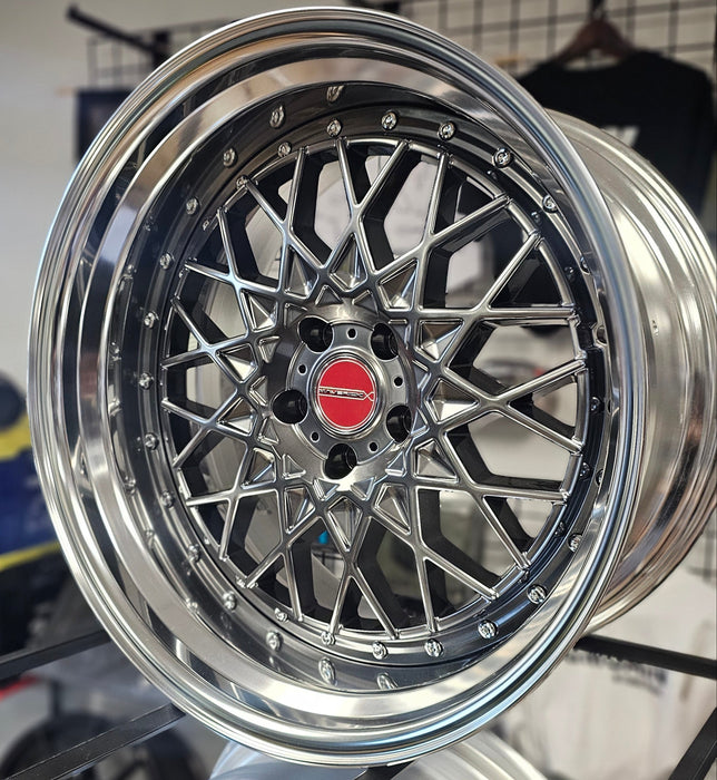 Close-up of a shiny silver car wheel rim with a red logo on a blurred background.