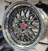 Close-up of a shiny silver car wheel rim with a red logo on a blurred background.